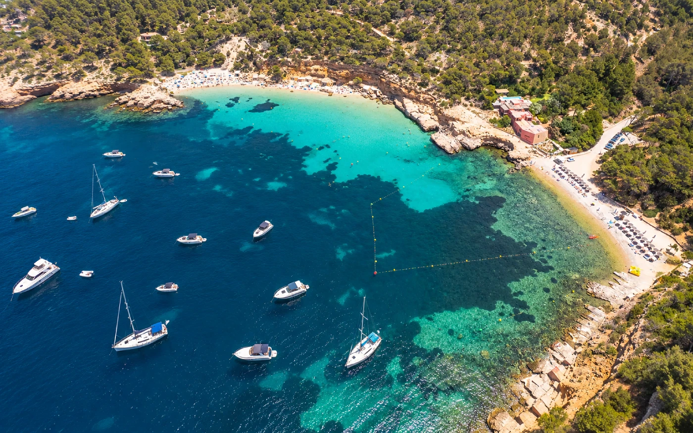 Boats anchored near Cala Salada and Cala Saladeta in Ibiza, seen from above with crystal-clear Mediterranean waters and protected swimming areas.